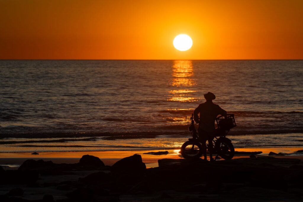 man with pushbike staring at sunset overlooking the ocean, high contrast