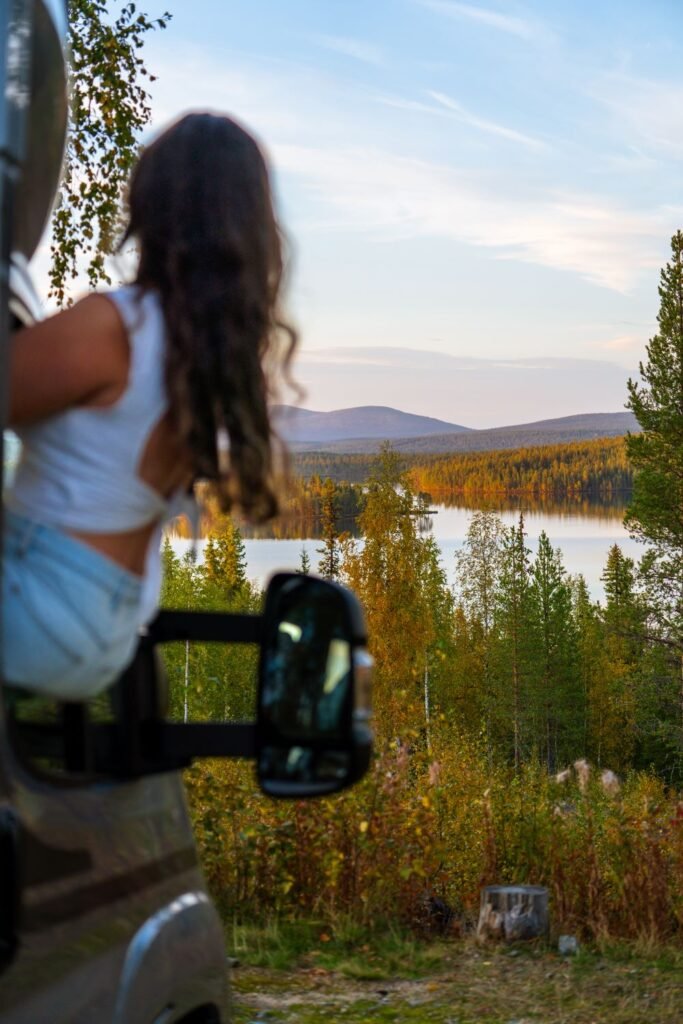 girl sitting out of campervan window staring at lake and forest in autumn