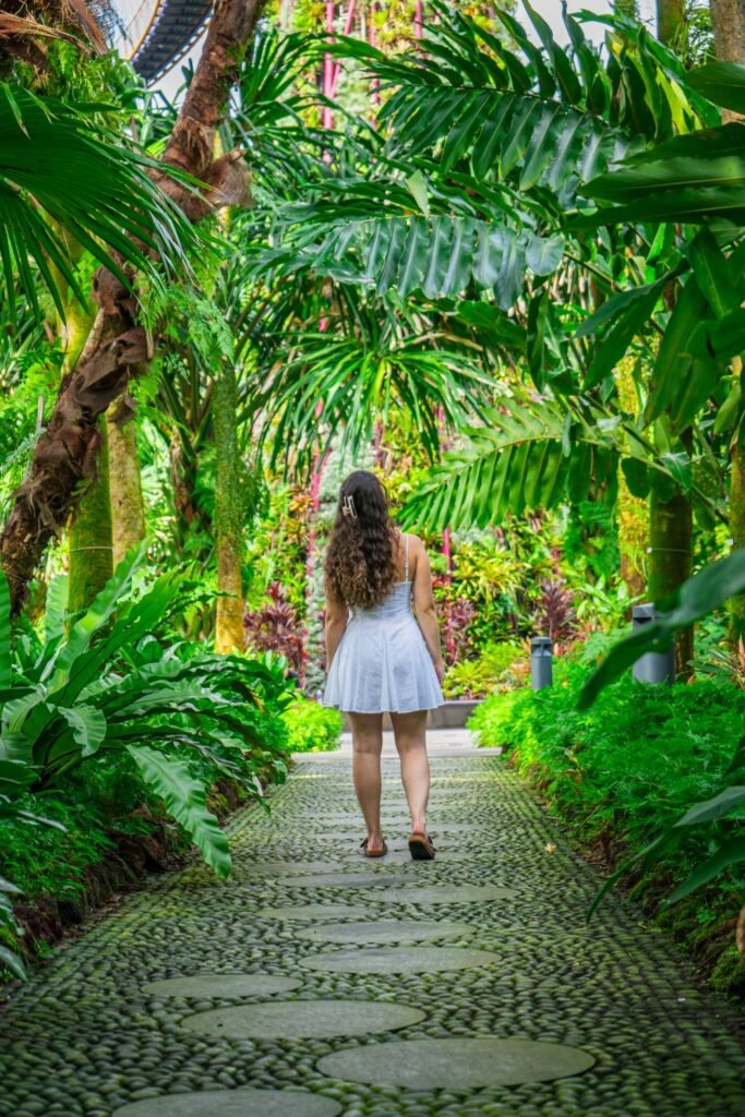 girl in foreground staring into thick, dense green forest gardens on cobblestone footpath