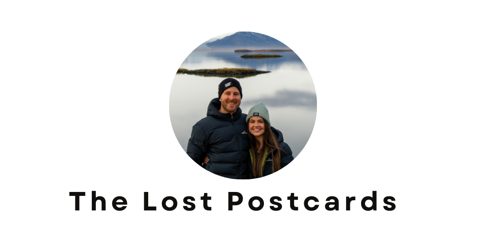 Couple standing in front of lake, islands in the background. Male and female are both wearing beanies and large jackets. Text underneath reads The Lost Postcards