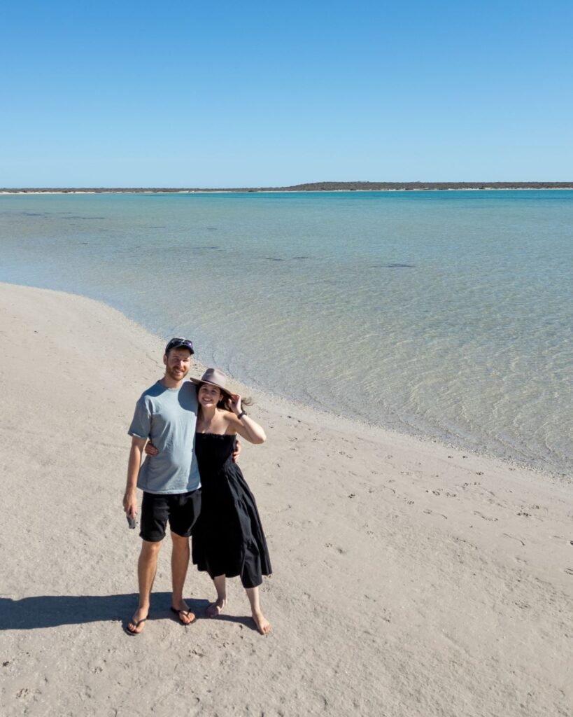 Couple standing in front of lagoon, white sand, midday