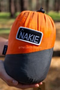 Person holding bag that reads Nakie, close up, orange top and black bottom packaging, Nakie written on front of bag