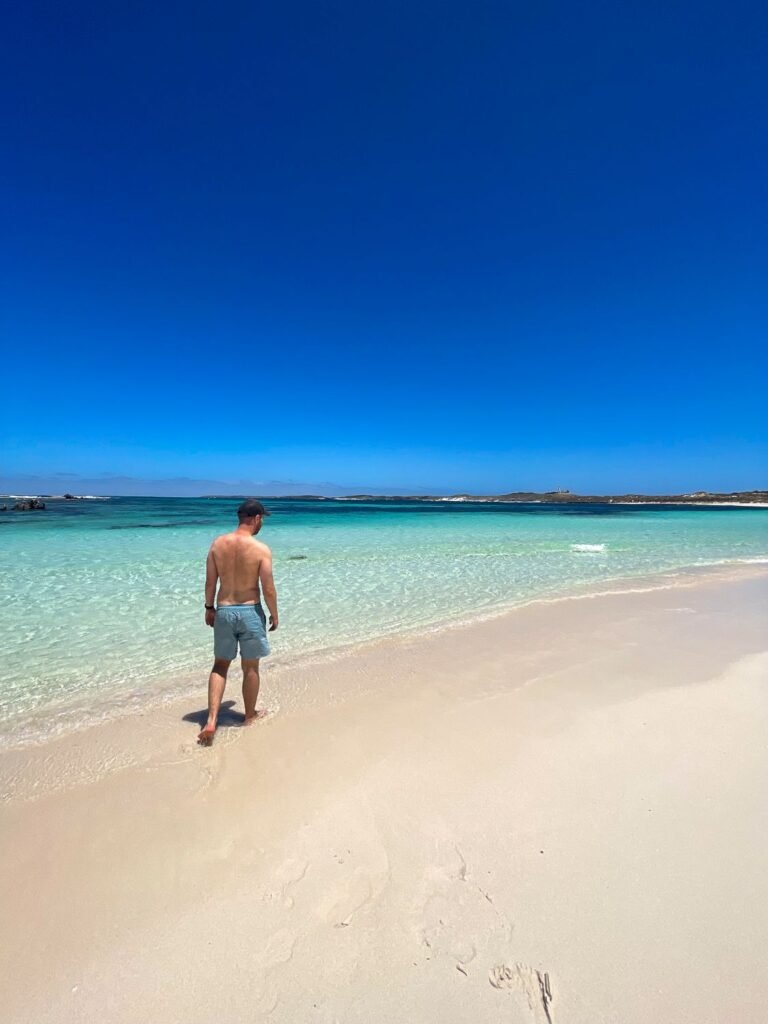 Person walking on beach, bright blue water, white sand