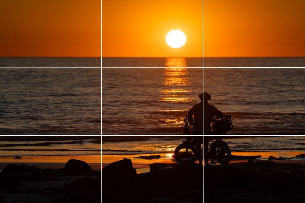 Man standing next to bicycle on beach, staring at beautiful sunset over the ocean, grid line overlay, how to take better photos using rule of thirds