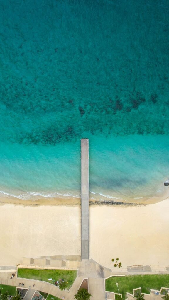 Top down image of jetty, bright white sand, bright blue ocean water