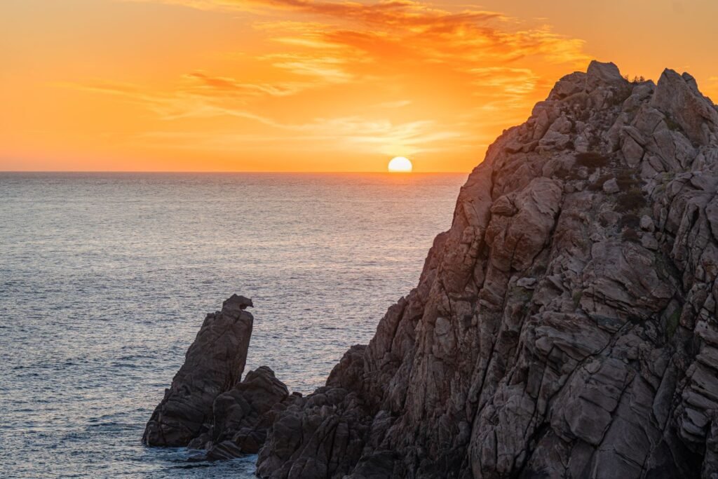 Very large rock island in ocean, bright orange sunset