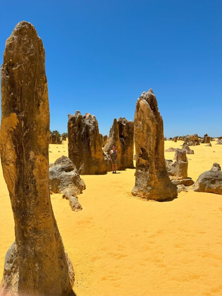 Large rock formations in yellow, sandy desert. Woman standing next to rocks. Places to visit in Western Australia.