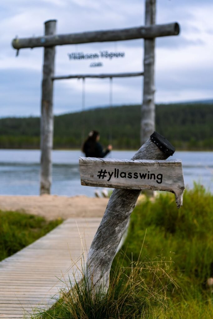 Sign that says #yllasswing, girl out of focus on wooden swing in background