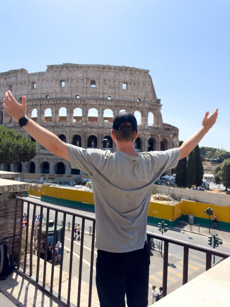 Man with arms outstretched standing looking at the Colosseum of Rome