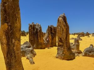 Large rock formations in yellow, sandy desert. Woman standing next to rocks.