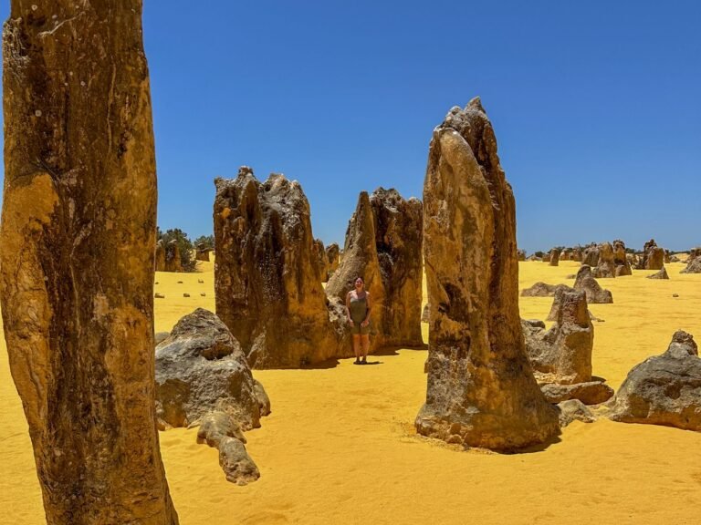 Large rock formations in yellow, sandy desert. Woman standing next to rocks.