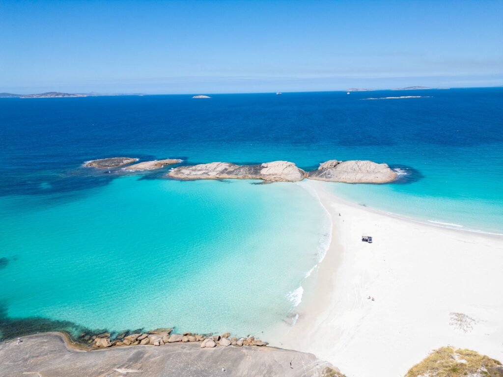 Large sand bank leading out to rock formations, crystal clear ocean on both sides